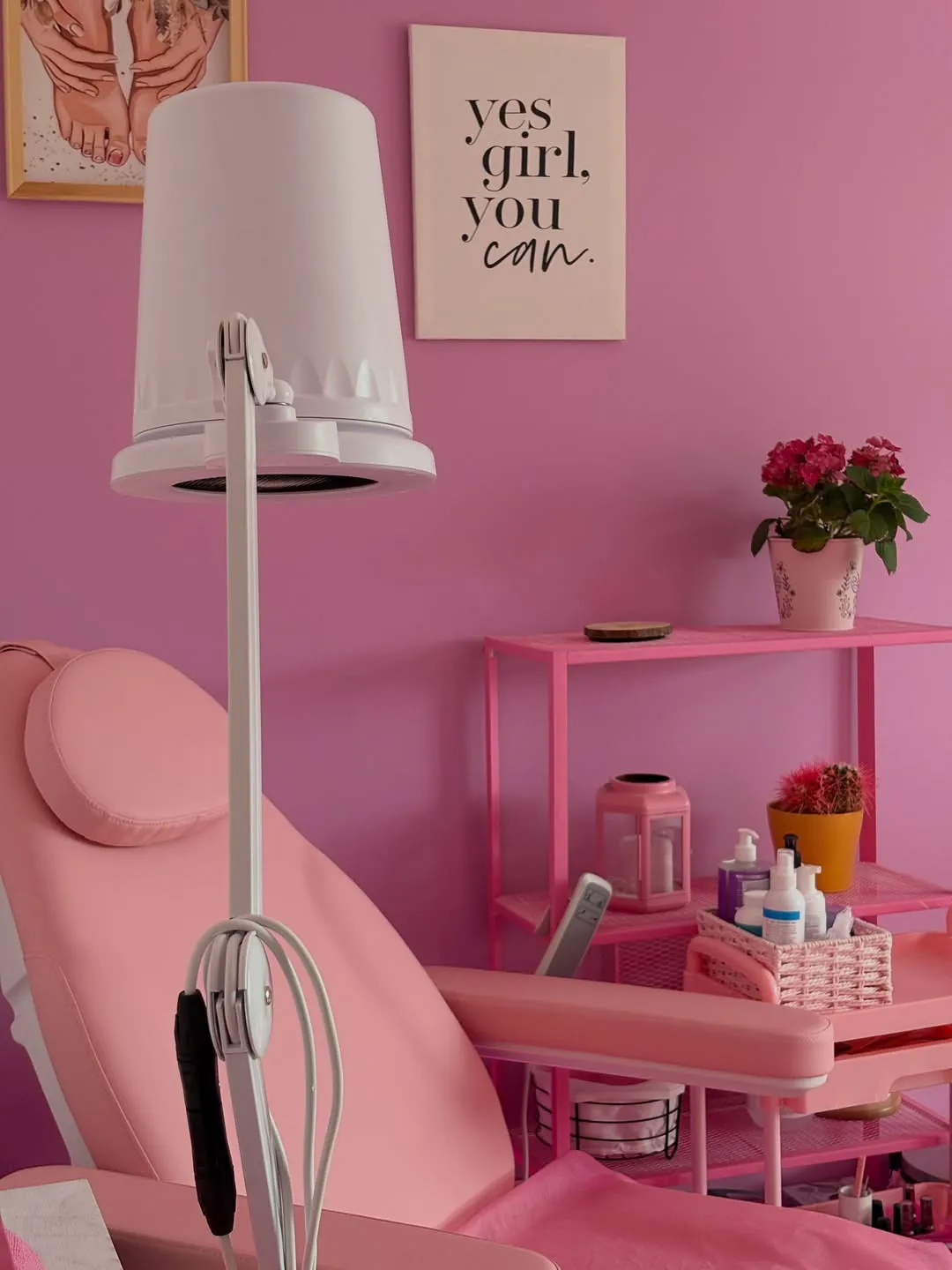 Rozā pedikīra krēsls ar lampu un plauktu, uz kura zied puķes